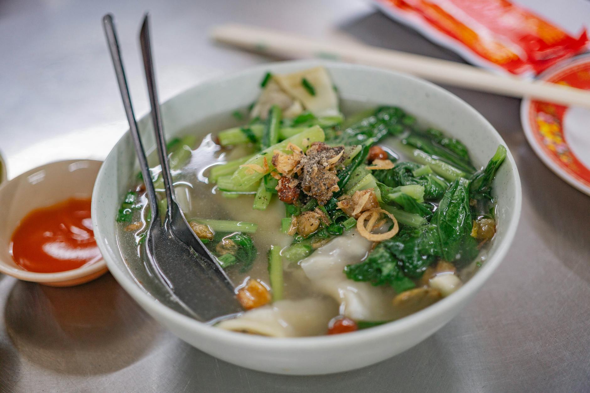 Miska azjatyckiej zupy warzywnej z pierożkami i świeżymi zieleninami