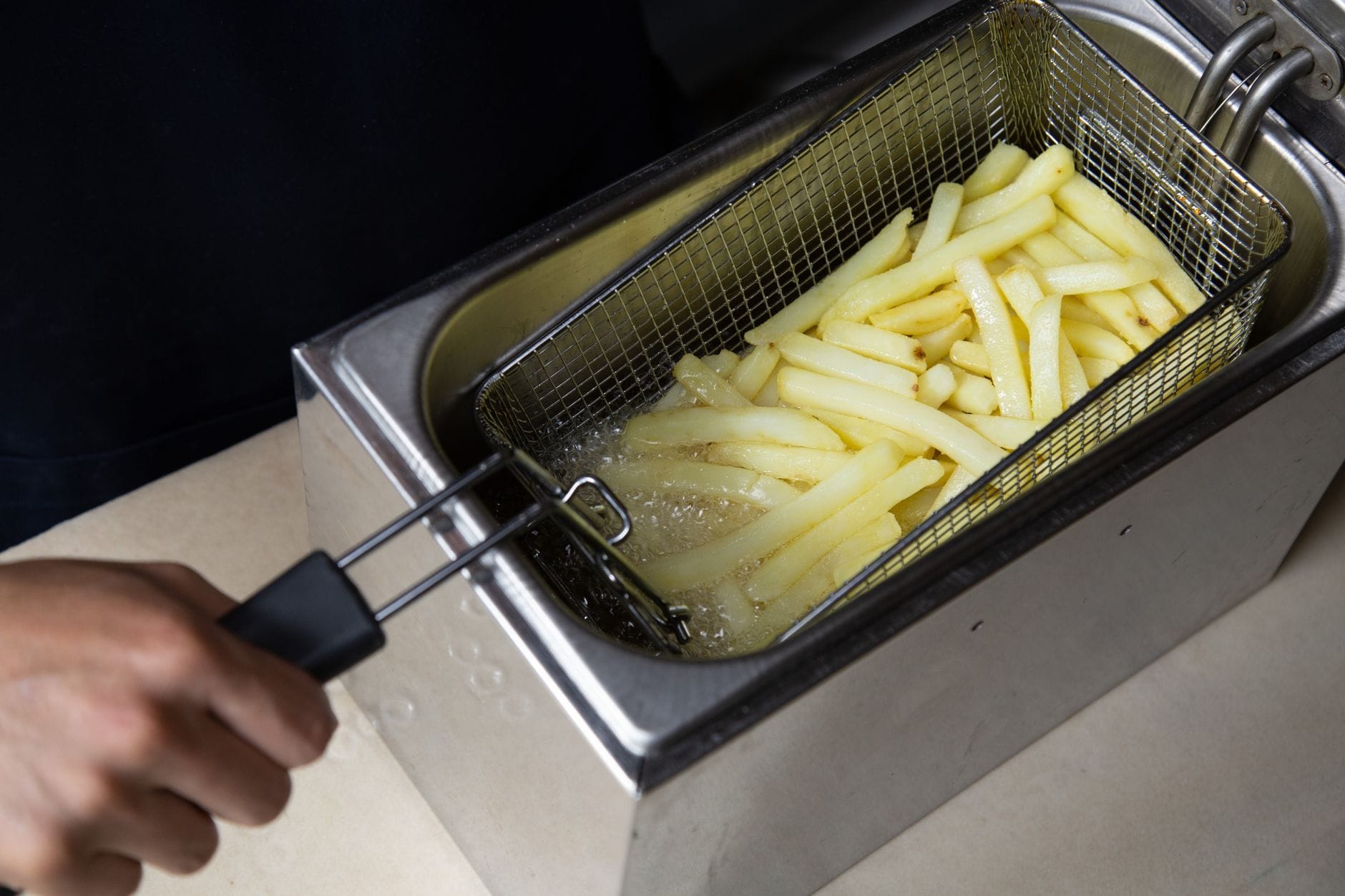 Zbliżenie na frytki smażone w głębokim oleju, dłoń trzyma kosz