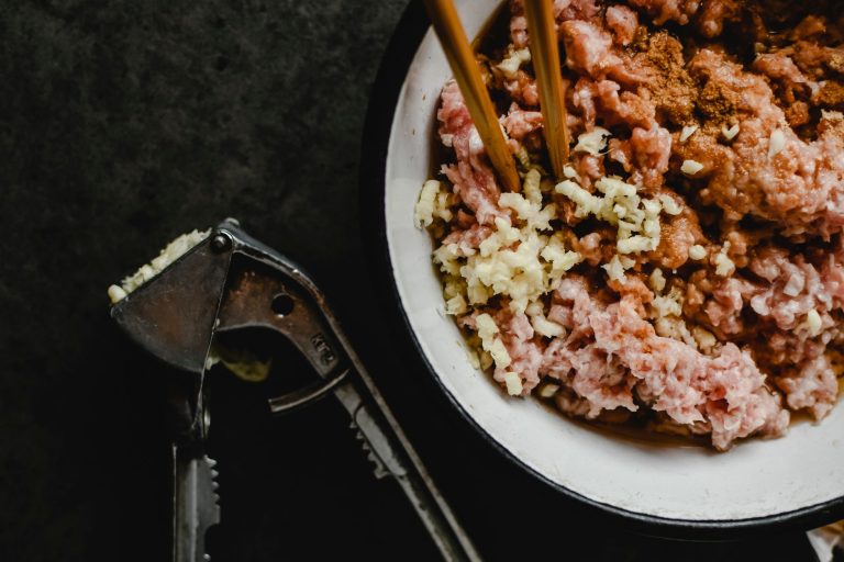 Surowe mięso mielone z czosnkiem i przyprawami w misce z pałeczkami
